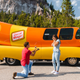 Man kneels with engagement ring in front of surprised girlfriend, with Oscar Mayer Wienermobile in the background